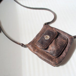 May include: A brown leather crossbody bag with a flap closure and a silver button. The bag has a small pocket on the front.
