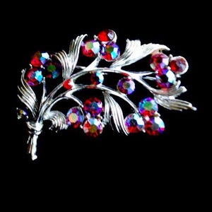 May include: A silver-toned brooch in a floral design, featuring iridescent red, purple, and blue crystal accents. The brooch has a branch-like structure with detailed leaves and round, colorful gemstones, set against a black background.