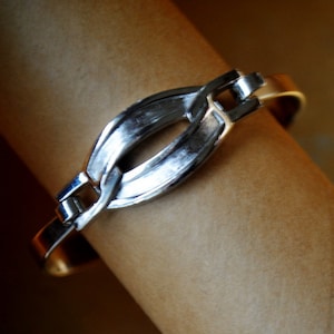 May include: A silver bracelet with a linked chain design and a large oval-shaped link in the center.