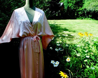 May include: A pink satin robe with embroidered floral details. The robe has a wrap style and a long, flowing silhouette.