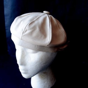 May include: A white beret with a button on top. The beret is made of a soft, smooth fabric.