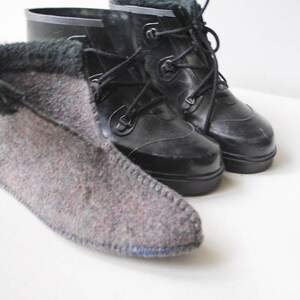May include: Black rubber boots with lace-up fastenings and a grey felt bootie with a dark green trim. The felt bootie is made of a grey and red speckled material. The boots are likely for cold weather, suitable for the winter.