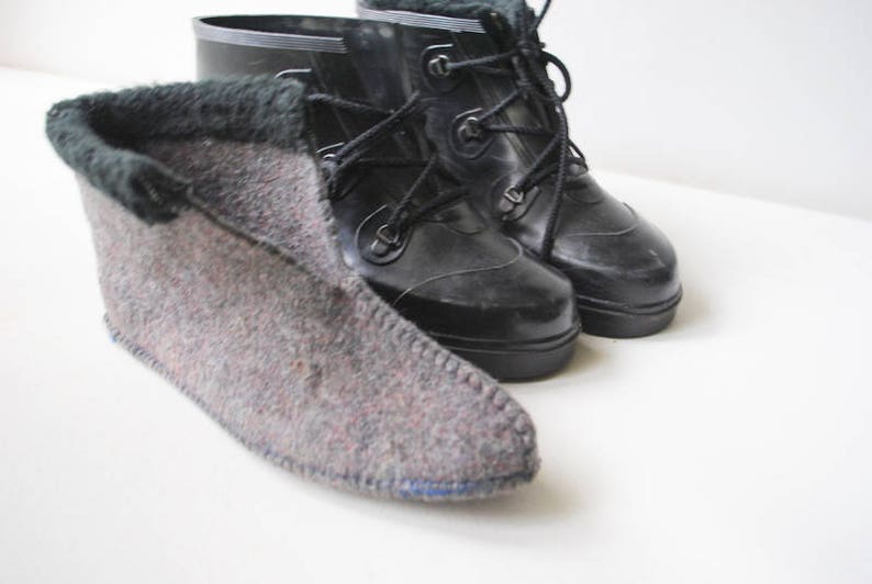 May include: Black rubber boots with lace-up fastenings and a grey felt bootie with a dark green trim. The felt bootie is made of a grey and red speckled material. The boots are likely for cold weather, suitable for the winter.