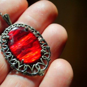 May include: A silver pendant necklace with a red, orange, and yellow gemstone set in a filigree design.