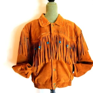 May include: A brown suede jacket with fringe detailing and blue and gold bead accents. The jacket has a button closure and a stand-up collar.