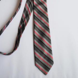 May include: A gray and red striped tie with a subtle sheen. The tie has a narrow width and a pointed tip.