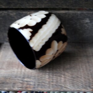 May include: A black and white bangle bracelet with a floral design. The bracelet is made of a hard, smooth material.
