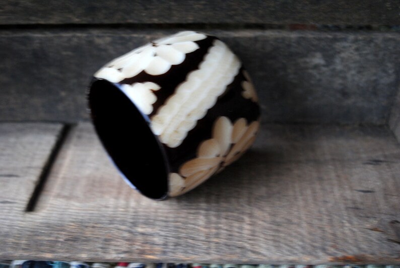 May include: A black and white bangle bracelet with a floral design. The bracelet is made of a hard, smooth material.