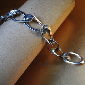 以下が含まれることがあります： ユニークなインターロックデザインのシルバーチェーンブレスレット。ブレスレットは留め金で留まります。