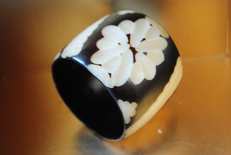 May include: A black and white bangle bracelet with a carved floral design. The bracelet is made of horn and has a polished finish.
