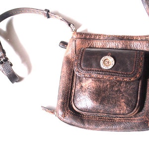May include: A brown leather crossbody bag with a flap closure and a silver button. The bag has a front pocket with a decorative stitch detail.