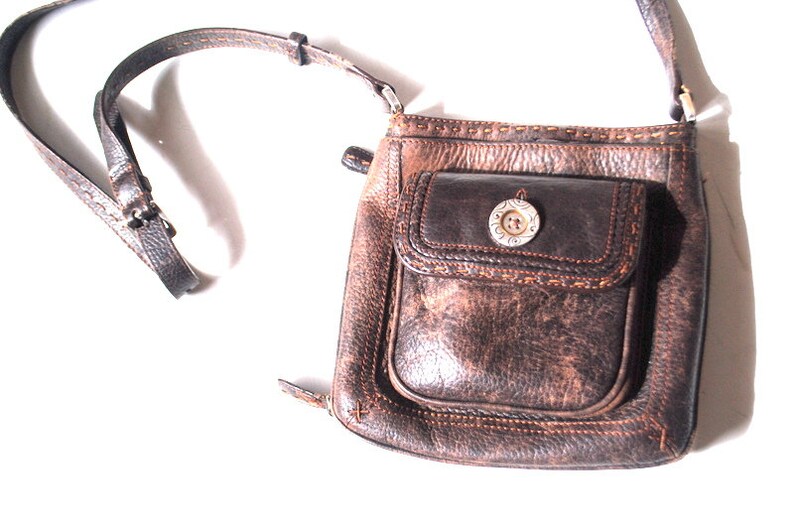 May include: A brown leather crossbody bag with a flap closure and a silver button. The bag has a front pocket with a decorative stitch detail.