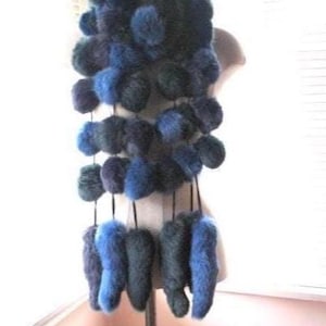 May include: A blue and teal fur scarf with a unique design. The scarf features multiple fur pom-poms and elongated fur pieces hanging from the main body. The color palette includes shades of blue and teal, creating a visually appealing accessory.