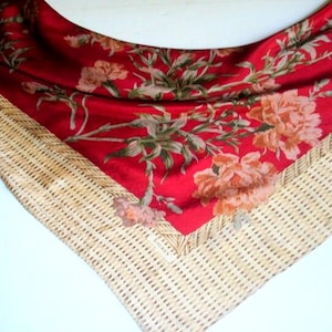 May include: A red silk scarf with a floral pattern and a woven border. The scarf features a vibrant red background with a design of peach and green flowers and leaves. The border is a light beige color.