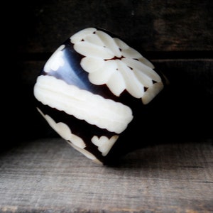 May include: A carved wooden bangle with a black and white floral design.