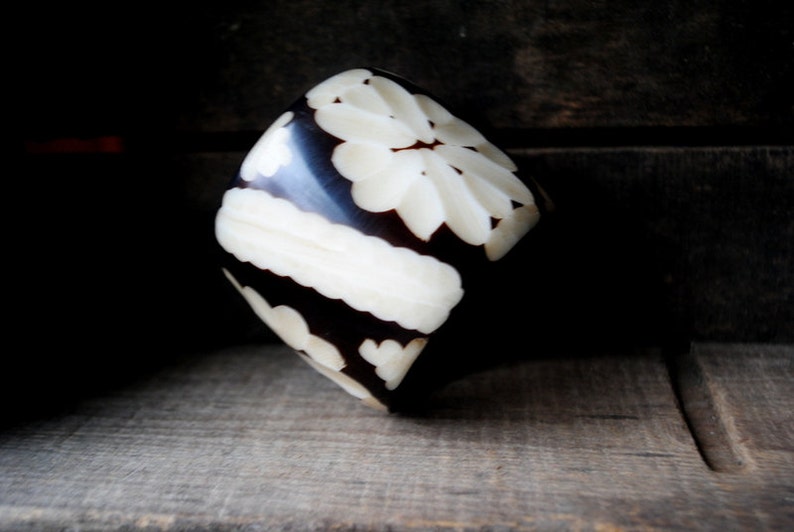 May include: A carved wooden bangle with a black and white floral design.