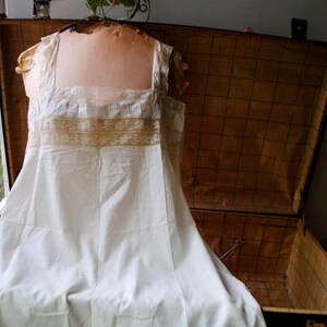 May include: A white cotton slip with lace trim. The slip is displayed on a mannequin and has a vintage look.