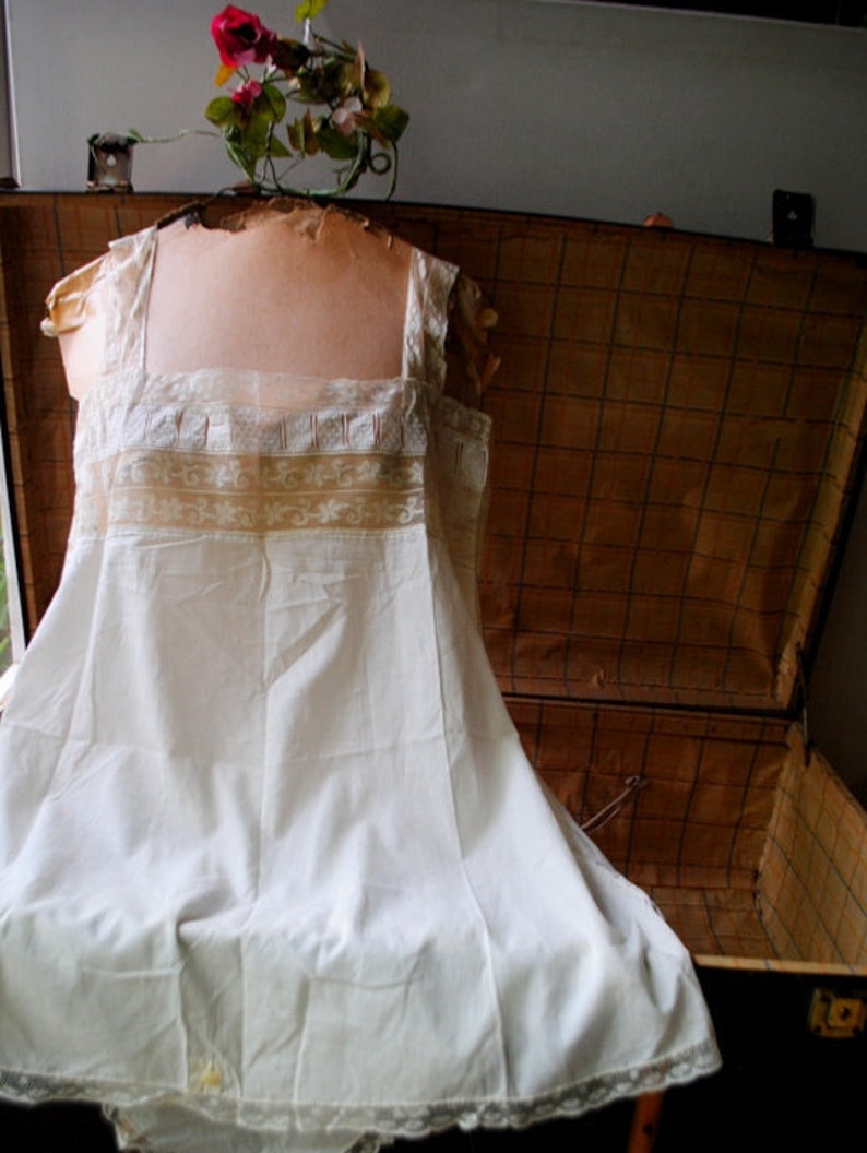 May include: A white cotton slip with lace trim. The slip is displayed on a mannequin and has a vintage look.