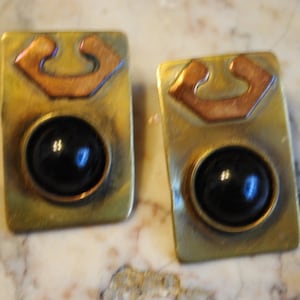 May include: A pair of gold tone earrings with a black stone and a copper colored design.
