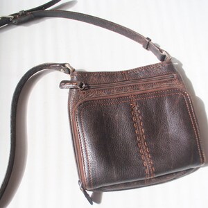 May include: A brown leather crossbody bag with a long adjustable strap. The bag has a flap closure and multiple pockets.