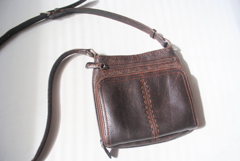 May include: A brown leather crossbody bag with a long adjustable strap. The bag has a flap closure and multiple pockets.
