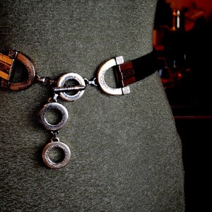 Peut inclure: Une ceinture noire avec une boucle argent&eacute;e et un d&eacute;tail de cha&icirc;ne. La boucle a un design unique avec plusieurs cercles et un fermoir d&eacute;coratif.