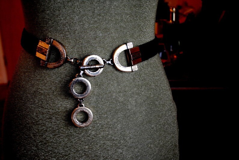 Peut inclure: Une ceinture noire avec une boucle argent&eacute;e et un d&eacute;tail de cha&icirc;ne. La boucle a un design unique avec plusieurs cercles et un fermoir d&eacute;coratif.