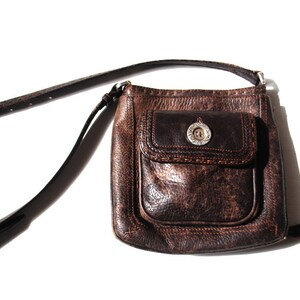 May include: A brown leather crossbody bag with a flap closure and a silver button. The bag has a front pocket with a decorative stitch detail.