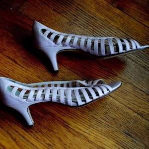 May include: A pair of lavender heeled sandals with a strappy design. The sandals have a pointed toe and a thin heel.