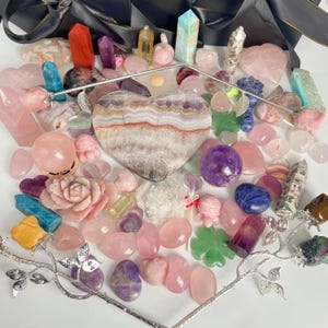 Puede incluir: Una colección de cristales y piedras rosas, moradas y verdes, incluyendo una gran amatista en forma de corazón, un cuarzo rosa y una variedad de otros cristales.