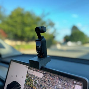 May include: A black camera with a screen is mounted on a black stand, which is attached to the top of a black computer screen. The screen is displaying a map with a search bar that says "Early Entry".