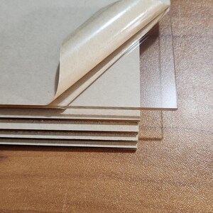May include: A stack of clear acrylic sheets with a brown paper backing. The paper is peeling back to reveal the sheets.