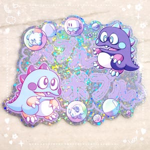 Pegatina Bubble Bobble: confeti holográfico de tamaño GRANDE con destellos y dinosaurios chibi en tonos morado pastel y azul y texto en katakana
