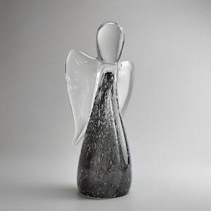 Könnte beinhalten: Eine klare Glasengel-Figur mit einem grau gesprenkelten Körper und klaren Flügeln. Der Engel hat einen tropfenförmigen Körper und einen Kopf mit einem haloartigen Detail. Die Flügel sind ausgebreitet.