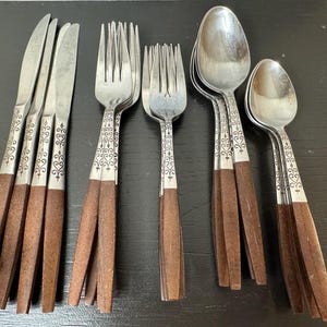 May include: A set of vintage silverware with stainless steel blades and tines, and spoons. The handles are a dark brown wood with a decorative silver design. The set includes knives, forks, and spoons, perfect for a formal dining setting.