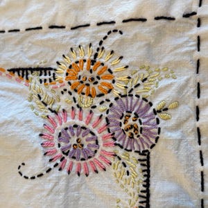 May include: White linen fabric with embroidered flowers in shades of pink, purple, orange, and yellow. The flowers are stitched in a detailed, intricate pattern.
