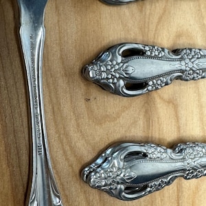 Op de afbeelding: Een set zilveren bestek met een bloemenmotief. De achterkant van een vork heeft de tekst "New York Cutlery Stainless" en "Imported" erop gedrukt.