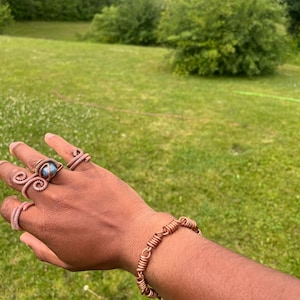 May include: A copper wire bracelet and three copper wire rings. One ring features a central blue stone, while the other two rings and the bracelet are constructed from coiled copper wire segments linked together in a continuous design.