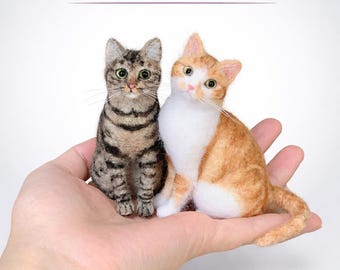 May include: Two handcrafted cat figurines, one tabby and one orange and white, are displayed. The tabby cat has green eyes and dark stripes. The orange and white cat has white paws and a pink nose. The text "Custom From Your Photo" is above the cats.