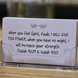 May include: A stack of white cards with black text in a clear plastic holder. The text reads, "When you feel faint, Kade, I WILL GIVE YOU POWER; when you have no might, I will increase your strength." The reference is Isaiah 40:29 & 41:10.