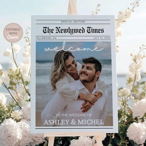 May include: A wedding welcome sign designed to look like a newspaper front page. The headline reads "The Newlywed Times" with the date July 16, 2026. The sign features a photo of a smiling couple and the names Ashley & Michel.
