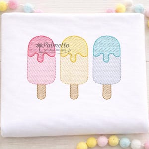 May include: Embroidered design of three colorful popsicles on a white background. The popsicles are pink, yellow, and blue, each with a dripping effect. The text "Palmetto Stitched Designs" is above the popsicles.