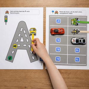 Könnte beinhalten: Zwei pädagogische Arbeitsblätter mit einer grauen Straße in Form des Buchstabens A und einem Parkplatzraster. Die Blätter enthalten kleine Spielzeugautos an Holzstäbchen, Ampelsymbole und Anweisungen mit dem Text Fahre mit dem Auto das A nach.