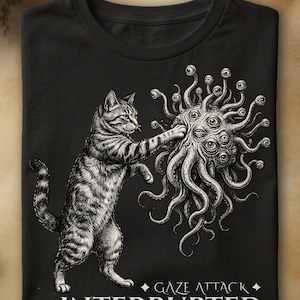 Peut inclure: Un t-shirt noir arborant une illustration blanche détaillée d'un chat tigré frappant une créature tentaculaire aux multiples yeux. Sous l'image, le texte GAZE ATTACK INTERRUPTED est inscrit en lettres blanches stylisées au centre.
