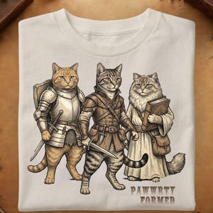 Peut inclure: Un t-shirt couleur crème avec une illustration graphique de trois chats habillés en aventuriers fantastiques. Un chat porte une armure de plaques avec un bouclier et une épée, un autre porte une tenue en cuir avec une dague, et le troisième porte des robes en tenant un livre. Le texte PAWWRTY FORMED est imprimé en dessous.