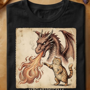 Peut inclure: Un t-shirt noir avec une illustration d'un dragon brun crachant du feu à côté d'un chat tigré orange debout. L'image a un fond de papier parchemin vintage. Sous le dessin, le texte indique : ZERO BRAIN CELLS MAXIMUM CONFIDENCE.