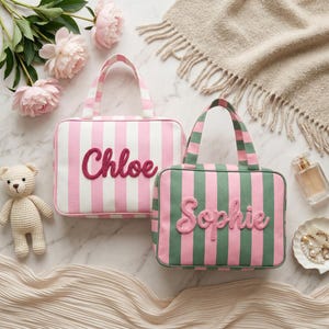 Könnte beinhalten: Zwei rechteckige Stofftaschen mit Tragegriffen und Streifenmuster. Eine Tasche hat weiße und rosa Streifen mit dem Namen Chloe in dunkelrosa Schreibschrift. Die andere Tasche hat grüne und rosa Streifen mit dem Namen Sophie in hellrosa Schreibschrift.