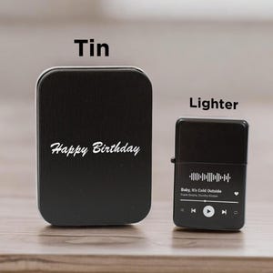 May include: Black tin with the text "Happy Birthday" and a black lighter with a song title and music player controls. The song title is "Baby, It's Cold Outside" by Frank Sinatra and  Doris Day.