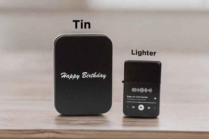 May include: Black tin with the text "Happy Birthday" and a black lighter with a song title and music player controls. The song title is "Baby, It's Cold Outside" by Frank Sinatra and  Doris Day.