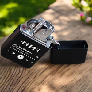 May include: A black lighter with a silver top and a white label that says "Baby, It's Cold Outside" with the song's artists, Frank Sinatra and Dorothy Kirsten, listed below. The label also includes a play button and a barcode.